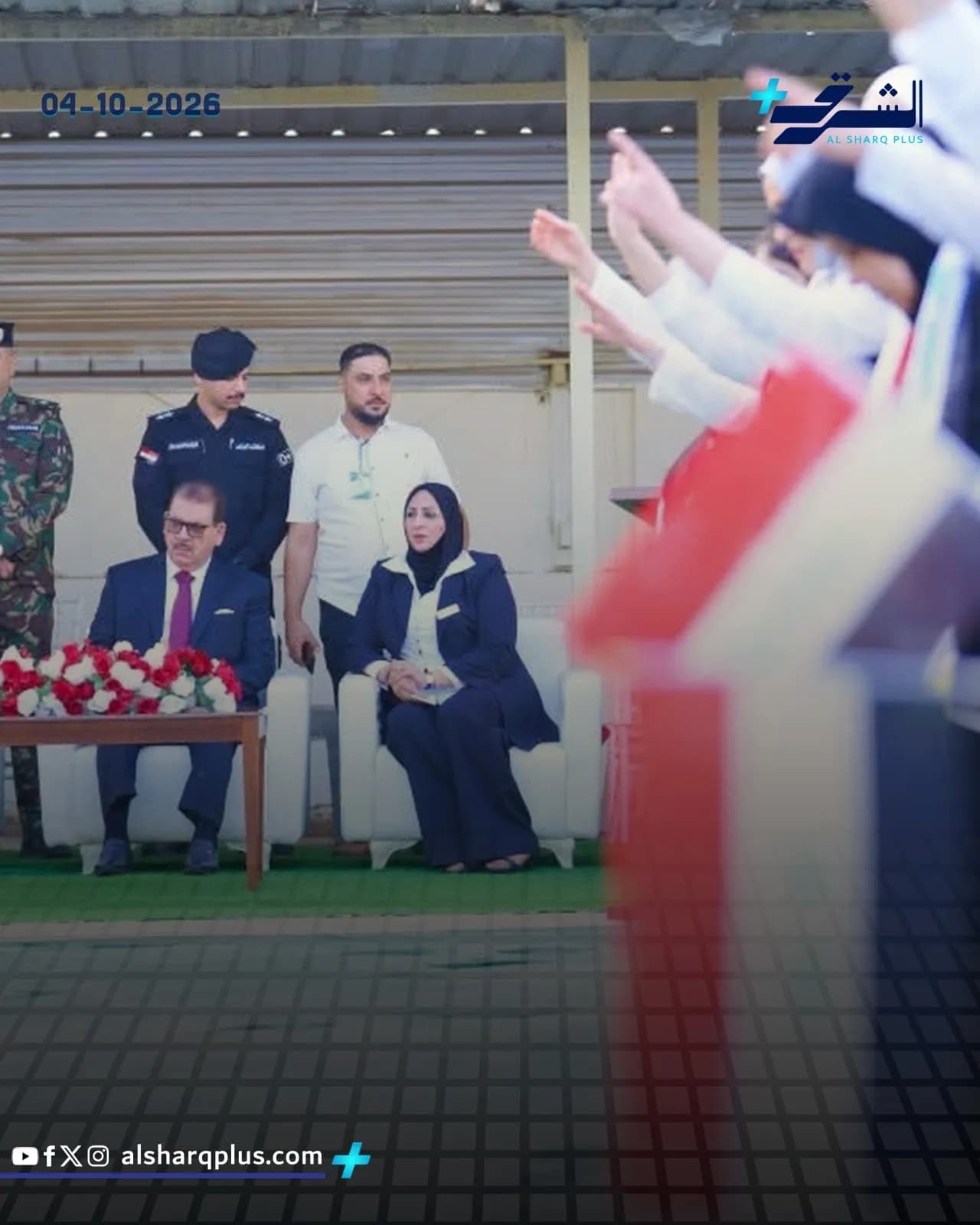 جمهور يحمل الأعلام ويصفق لمسؤولين يجلسون على اليسار في حدث عام.